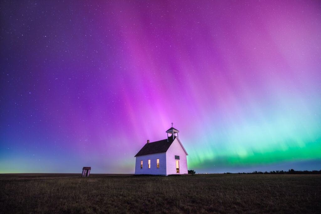The northern lights shining in purple, pink, blue, and green above Abbott Church in the middle of the night.