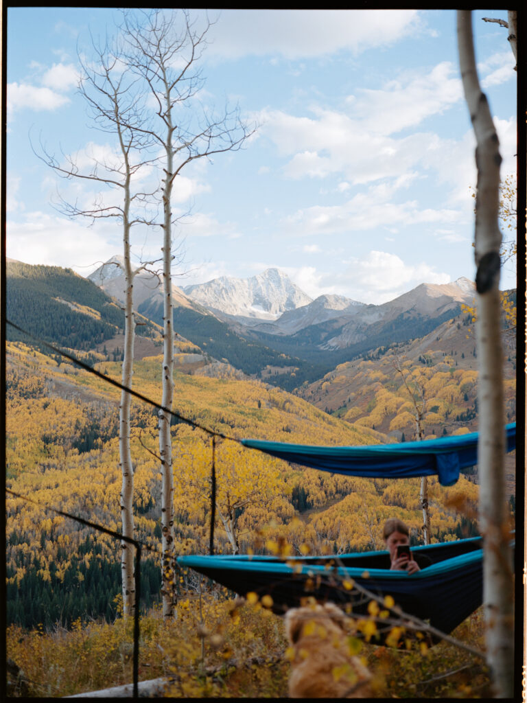 Two hammocks strung across aspen trees in Maroon Bells Wilderness. Capitol Peak behind, with the valley full of yellow aspen trees