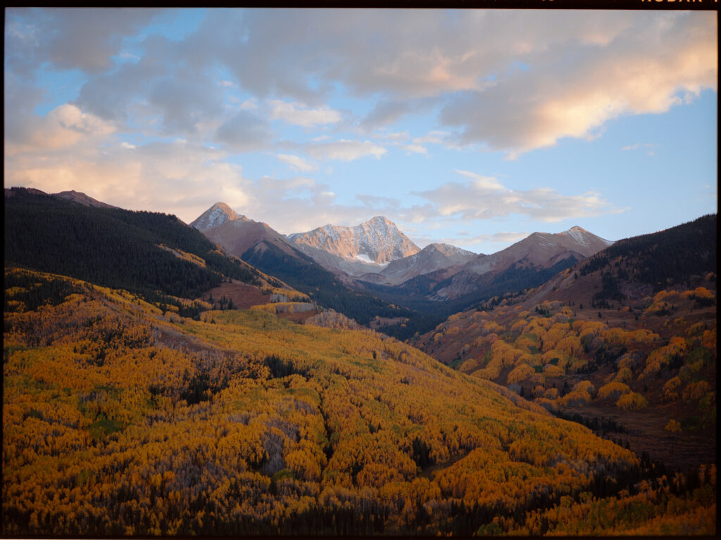 A sunset and alpenglow above Capitol Peak In Maroon Bells Wilderness, a valley of bright fall colors cascading below