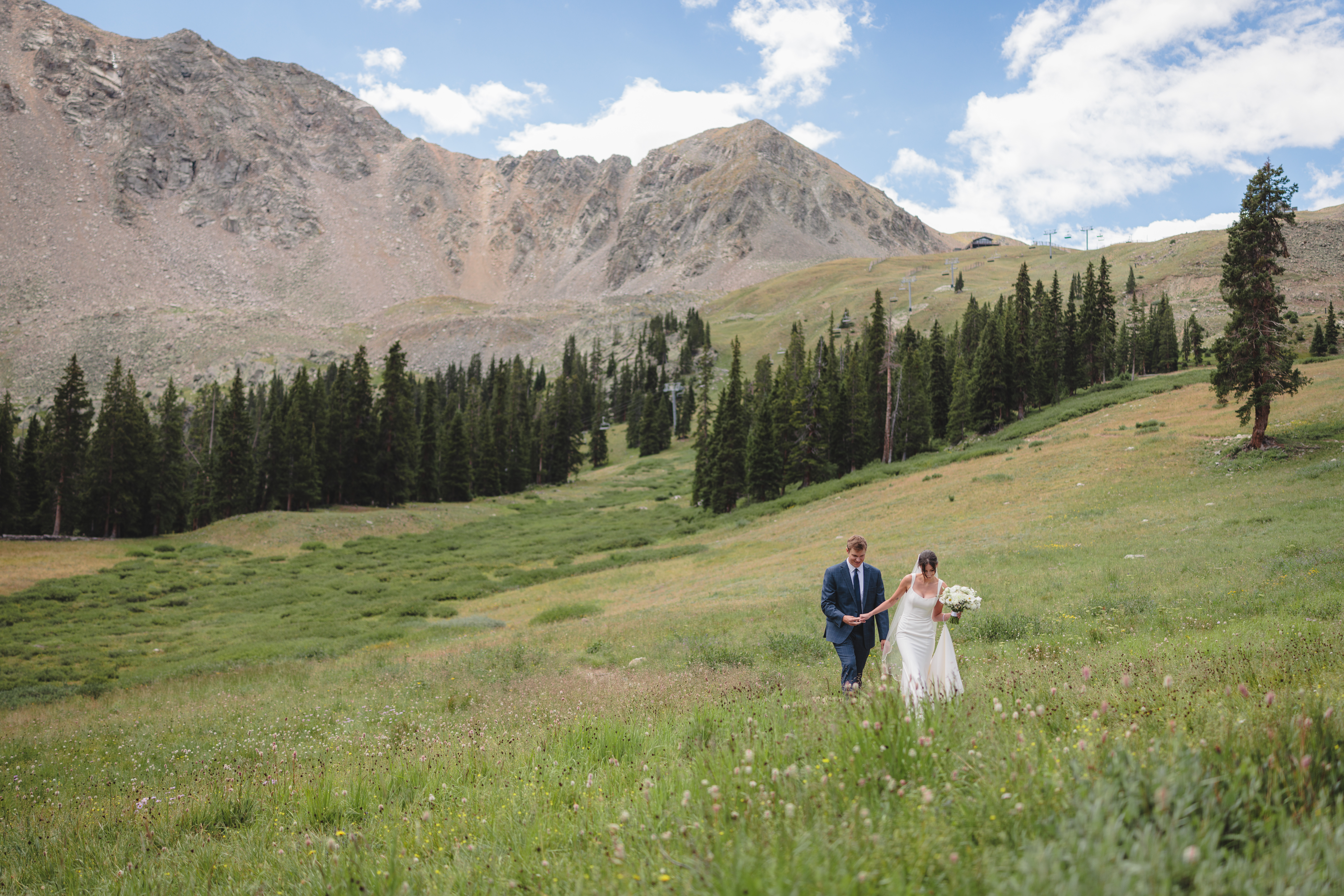 A couple on their wedding day walking through a field at A-Basin Ski Resort